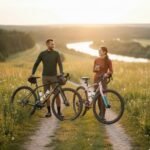 Mann steht mit einem grünen Herren Gravelbike der 2026 Kollektion auf einem Schotterweg in einer hügeligen Landschaft bei Sonnenuntergang